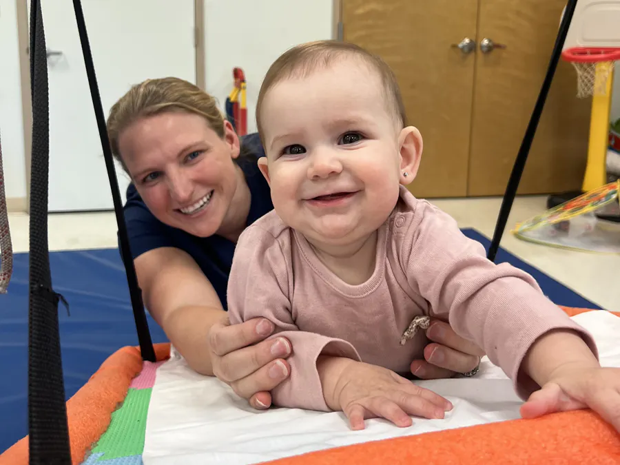 A child smiling on a swing while receiving physical support from a therapist.